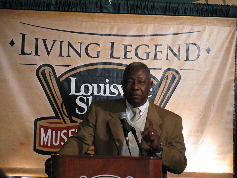 I picture of Hank Aaron in a suit and tie giving what appears to be a speech.