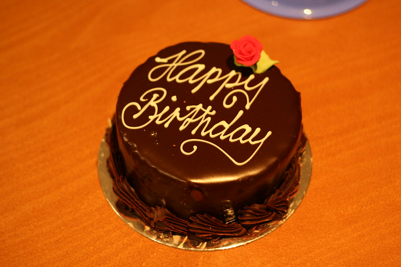 A round birthday cake with chocolate icing, "Happy Birthday" inscribed.