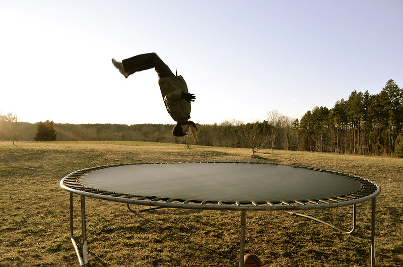 A person doing a flip on a trampoline in a field.