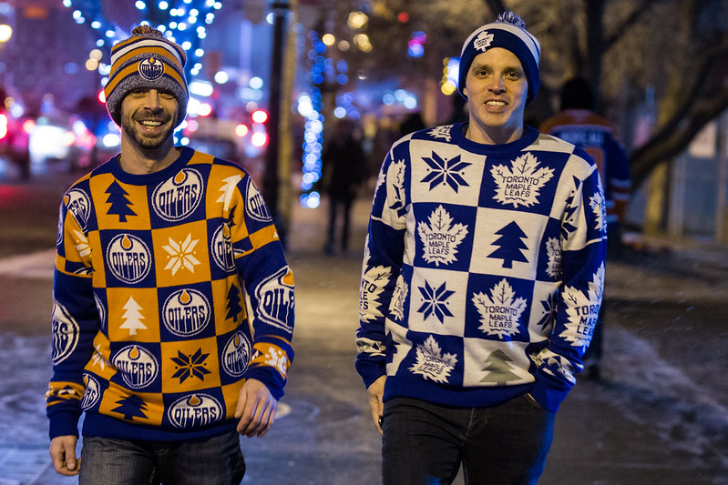 Two young men walking in Edmonton; one wearing #Oilers sweather and tuque, the other with #MapleLeafs sweater and tuque.