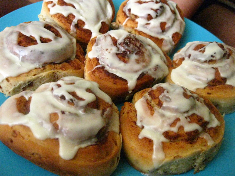 Seven cinnamon rolls with a glaze on a blue plate.