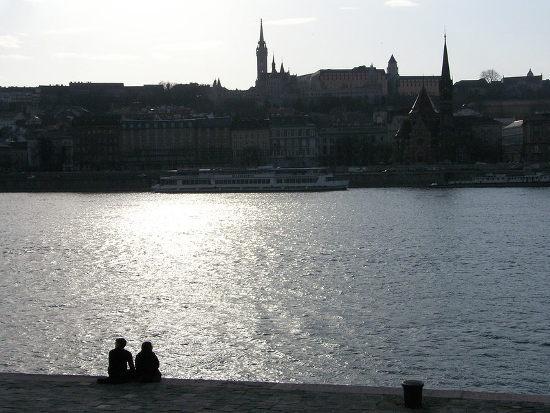 A couple sitting on a pier at the river through Budapest.