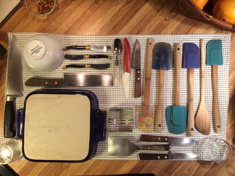 “When one gets (crossed out)bored creative while doing the dishes”. Dishes laid out to dry on a towel, mainly knives and spatulas.