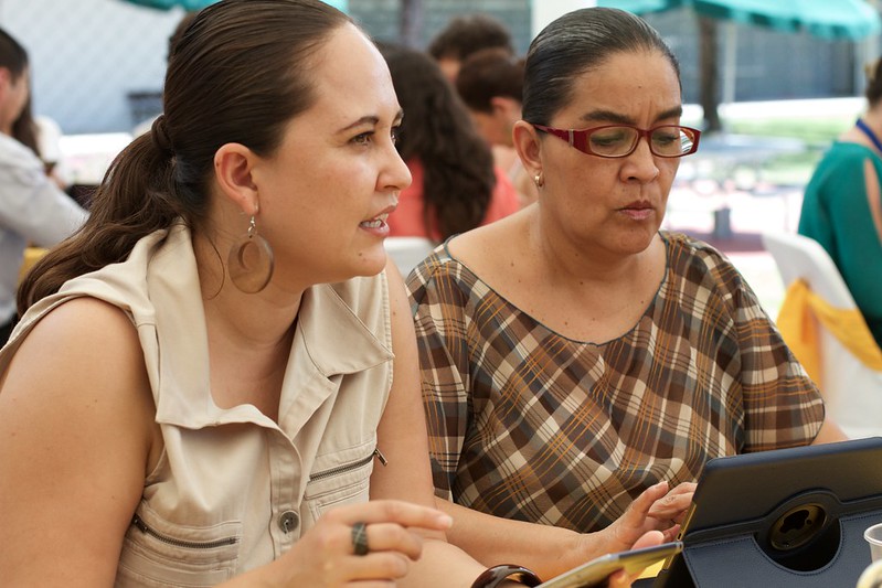 Closeup of two teachers in conversation with others in the background.