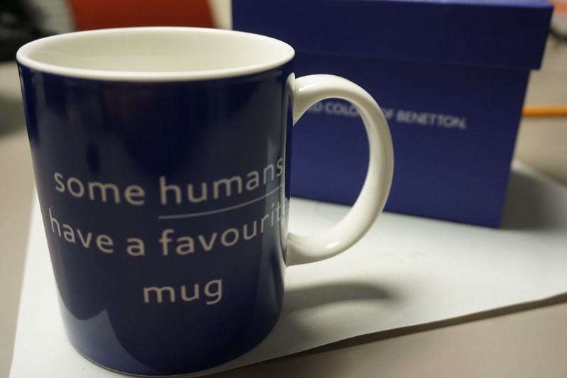 Picture of a mug with a blue box behind it that is out of focus. The mug reads "some humans have a favourite mug".
