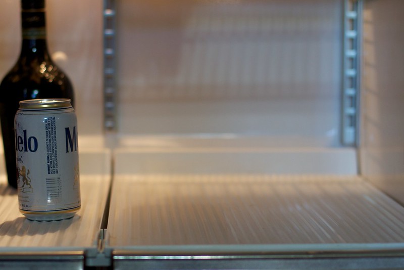 Pict ure of an almost empty fridge shelf. Modelo beer can in the foreground with another bottle of something behind it.