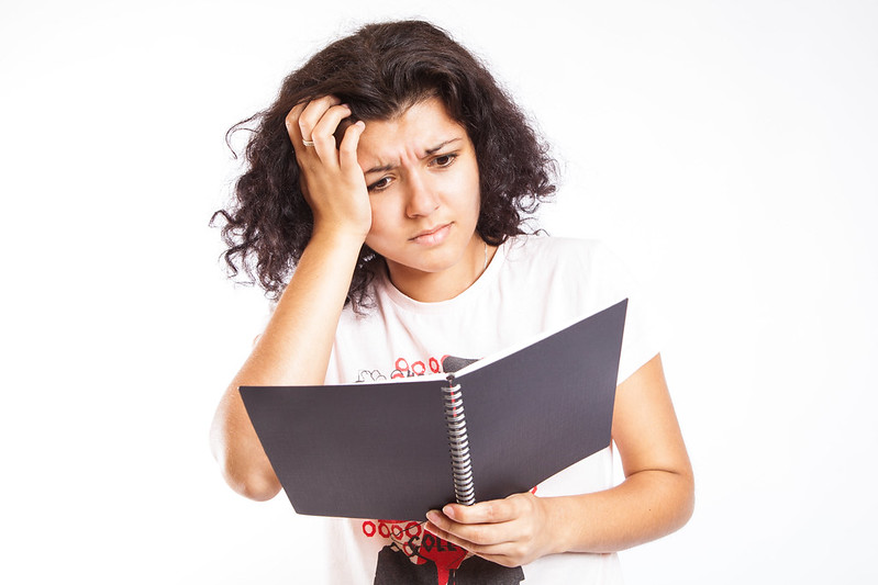 Young woman scratching her head while looking confused at a binder of class notes.
